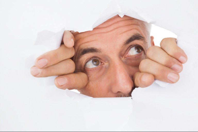 Close up of mature man peeking through torn white surface