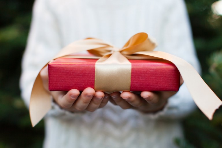 close-up of nicely wrapped christmas gift being held by a child with no face visible, christmas tree in the background, christmas time concept
